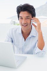 Smiling man using his laptop and talking on phone