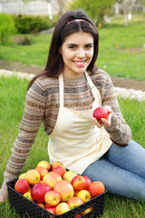 Portrait of smiling woman with basket apples against green grass