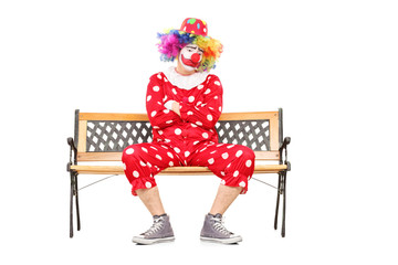 Unhappy clown sitting on a wooden bench