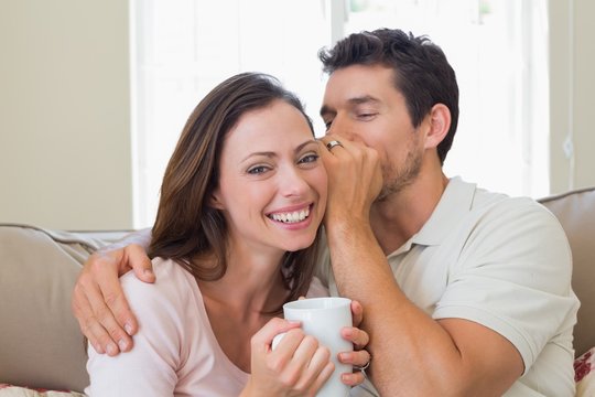 Man whispering secret into a womans ear in living room