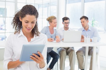 Casual businesswoman using tablet with team behind her