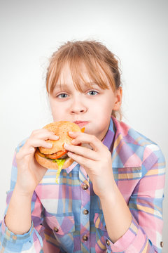 Little blond girl eats burger above white wall