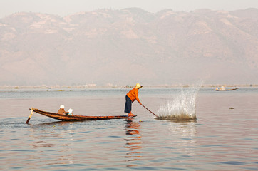 Fisherman drives fish into nets using a stick. Inle Lake.
