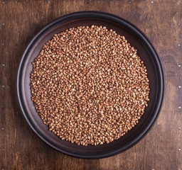 Organic buckwheat groats in plate on dark wood background