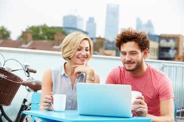 Young Couple Sitting On Roof Terrace Using Laptop