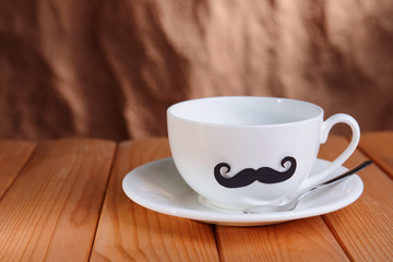 Cup with mustache on table on brown background