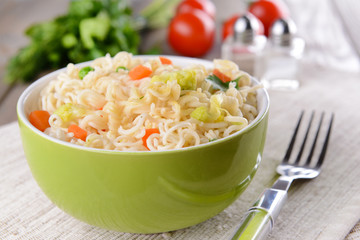 Tasty instant noodles with vegetables in bowl on table close-up