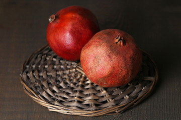 Ripe pomegranates on wicker mat, on wooden background