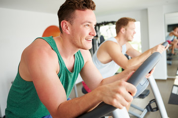 Two Young Men Training In Gym On Cycling Machines Together