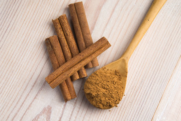 Cinnamon, whole sticks behind wooden spoon with a heap of powder
