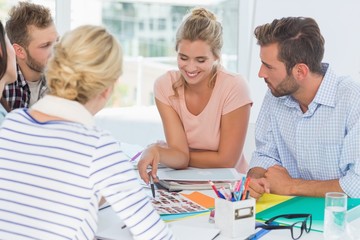 Obraz premium Uśmiechnięty zespół projektowy przeglądający arkusze kontaktowe na spotkaniu