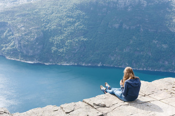 Fototapeta premium Woman sitting on Pulpit Rock / Preikestolen, Norway