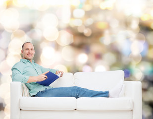 smiling man lying on sofa with book