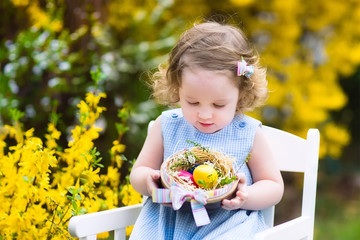 Beautiful curly toddler girl enjoying easter egg hunt in garden