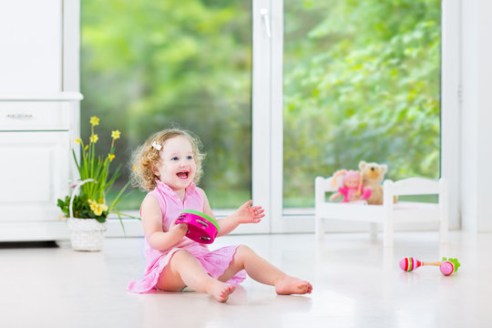 Little Toddler Girl Playing Tambourine In White Nursery