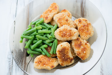 Glass plate with chicken nuggets and beans, wooden background