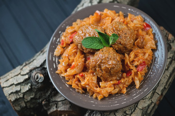 Glass plate with braised cabbage and meatballs on wooden logs