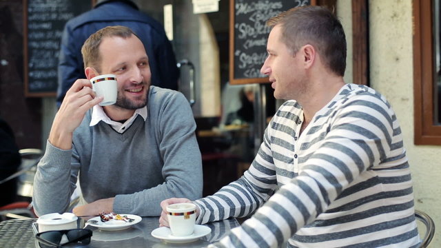 Two male friends drinking coffee and chatting in cafe
