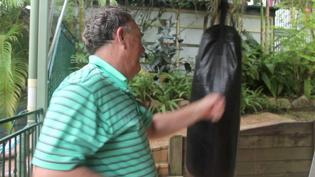 Middle aged man works out with a punching bag.
