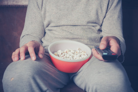Young man watching television and eating popcorn