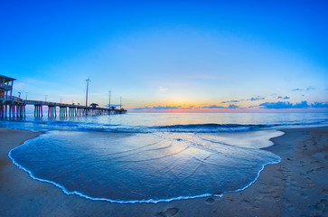 The rising sun peeks through clouds and is reflected in waves by