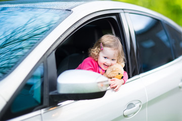 Cute laughing toddler girl in a car with a teddy bear