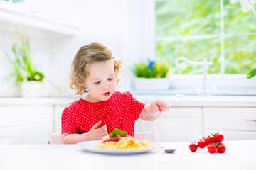 Funny toddler girl eating spaghetti in white kitchen