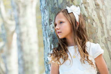 Girl in white standing next to tree.