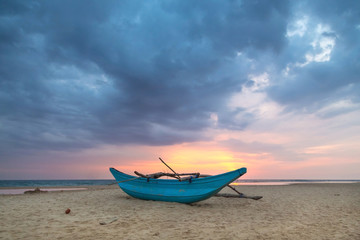 Traditional Sri Lankan fishing boat on empty sandy beach.