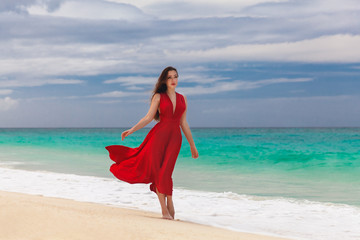 Beautiful woman in a red dress  standing on the sea coast