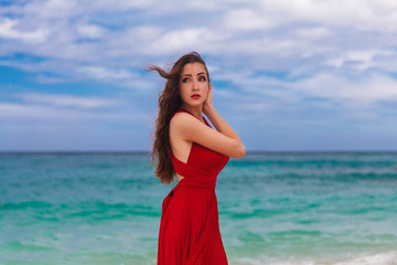 Fototapeta na wymiar Beautiful woman in a red dress standing on the sea coast