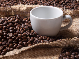 white cup with coffee on burlap background with beans