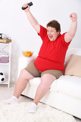 Fototapeta na wymiar Lazy overweight male sitting on couch and watching television