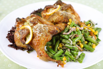 Roasted quails with vegetables on plate, on wooden background