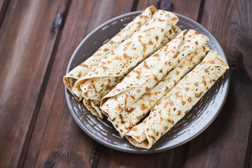 Glass plate with rolled crepes, wooden background, studio shot