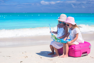 Little lovely girls sitting on big suitcase and a map at