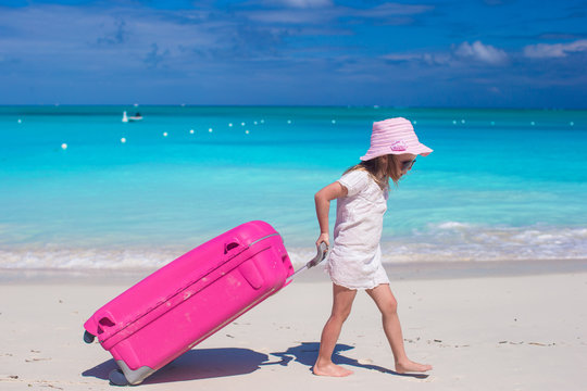 Little adorable girl with big colorful suitcase in hands walking
