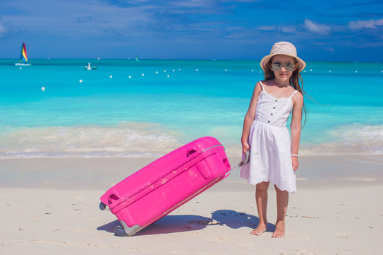 Little adorable girl with big colorful suitcase in hands on