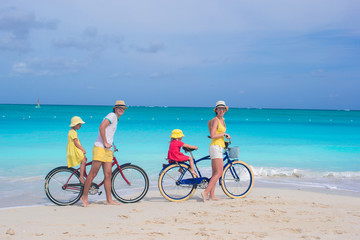 Fototapeta premium Young parents and little girls with bikes on a tropical white