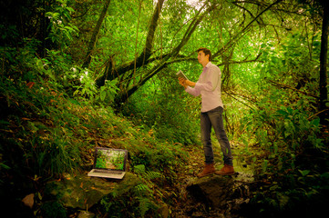 man using tablet with laptop in the forest