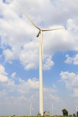 Wind turbine on the green grass over the blue clouded sky