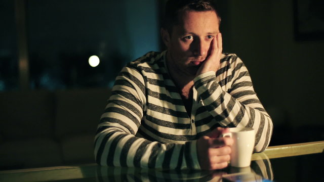 Pensive, thoughtful man sitting by the table in dark room 