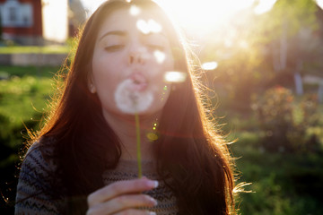 Beautiful woman blowing on dandelion in the garden