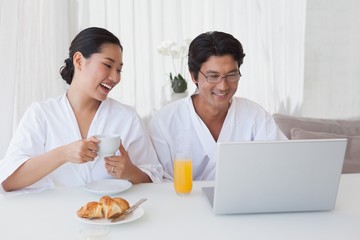 Happy couple using laptop over breakfast