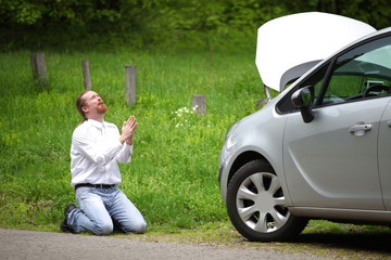 Funny driver praying a broken car by the road - 64321379