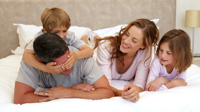 Cute parents and children lying on bed joking