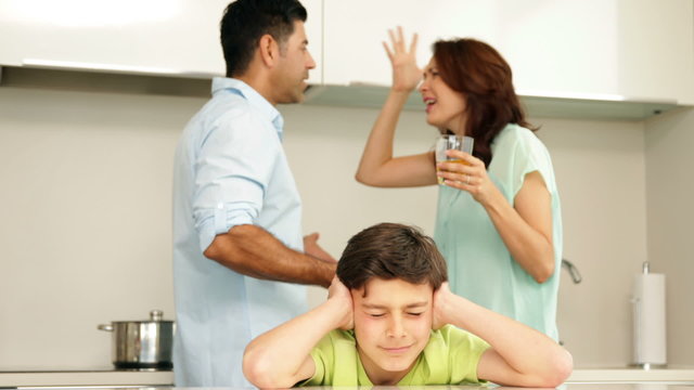 Upset boy covering his ears while his parents fight