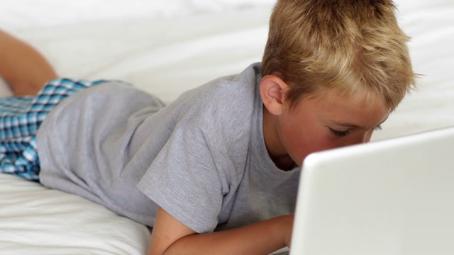 Little boy using laptop on bed