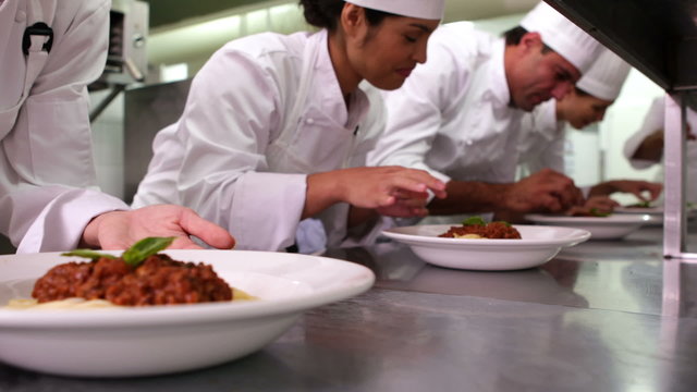 Row of chefs garnishing spaghetti dishes