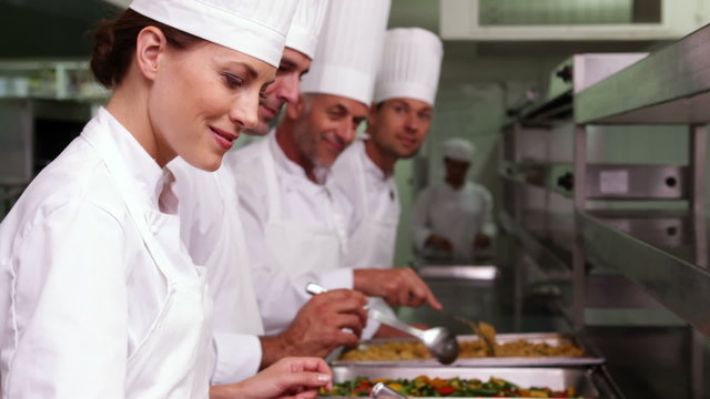 Row of chefs preparing food in serving trays